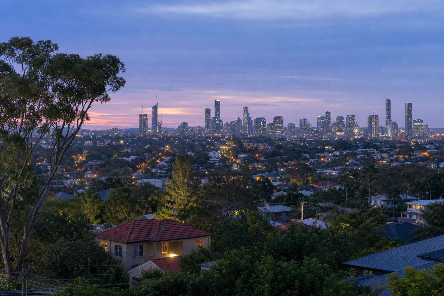 Australian city skyline beyond leafy inner-suburb houses at dusk